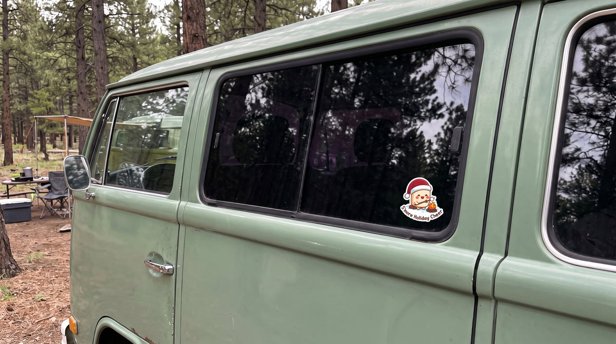 S'more Holiday Cheer sticker from the Holiday Survival bundle on a green camper van window at a forest campsite
